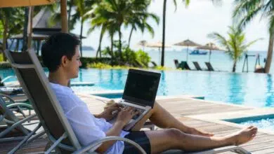 Asian man spent his summer vacation working on his laptop in a chair near the swimming pool in resort hotel near sea.