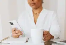 A person checking their email on an iphone and drinking coffee.