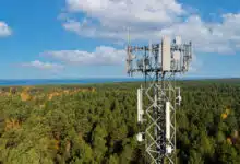 telecommunication tower with antennas for 5g network on forest and blue sky background