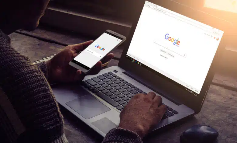 Man using both his laptop and mobile phone with Google on display.