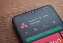 Asana app play store page on the display of a black mobile smartphone on wooden background